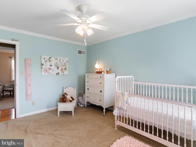 carpeted bedroom with a crib, ornamental molding, and ceiling fan