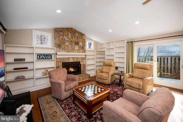 living room featuring hardwood / wood-style flooring, vaulted ceiling, a stone fireplace, and a wealth of natural light