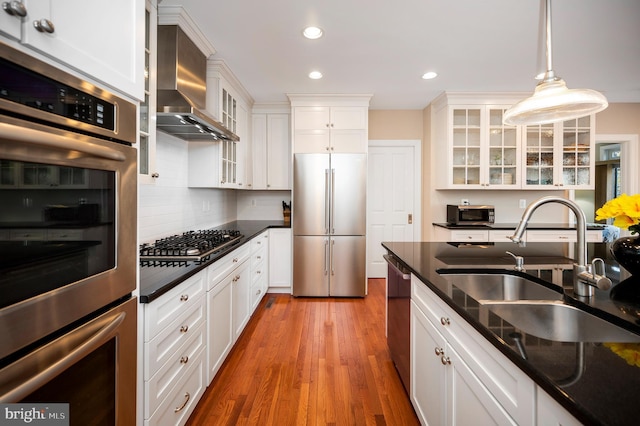 kitchen with white cabinets, appliances with stainless steel finishes, hanging light fixtures, and wall chimney range hood