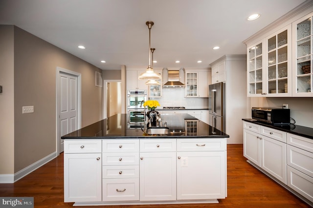 kitchen with stainless steel appliances, an island with sink, sink, and wall chimney range hood