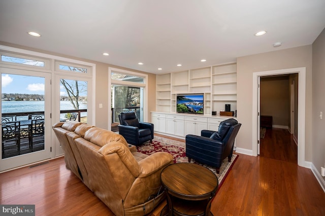 living room with built in shelves, wood-type flooring, and a water view