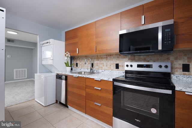 kitchen featuring stacked washer and dryer, sink, tasteful backsplash, light tile patterned floors, and appliances with stainless steel finishes