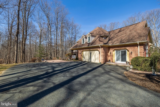 view of property exterior with aphalt driveway, brick siding, a garage, and a shingled roof