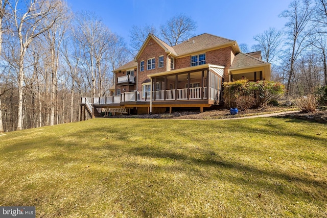 back of house featuring a wooden deck, brick siding, a lawn, and a sunroom