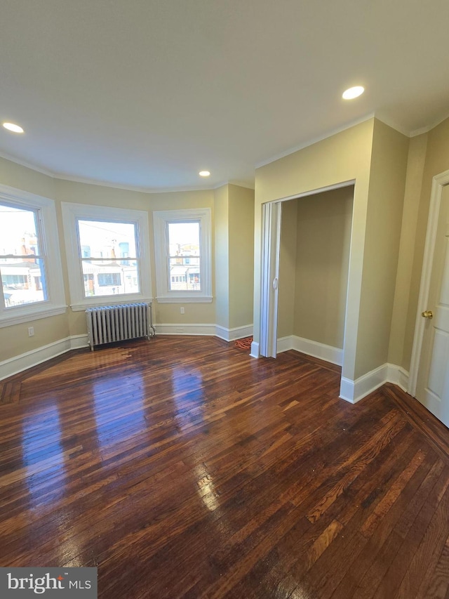 unfurnished room featuring dark wood-type flooring, radiator heating unit, and crown molding