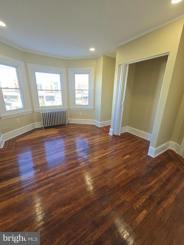 spare room featuring dark wood-type flooring, ornamental molding, and radiator