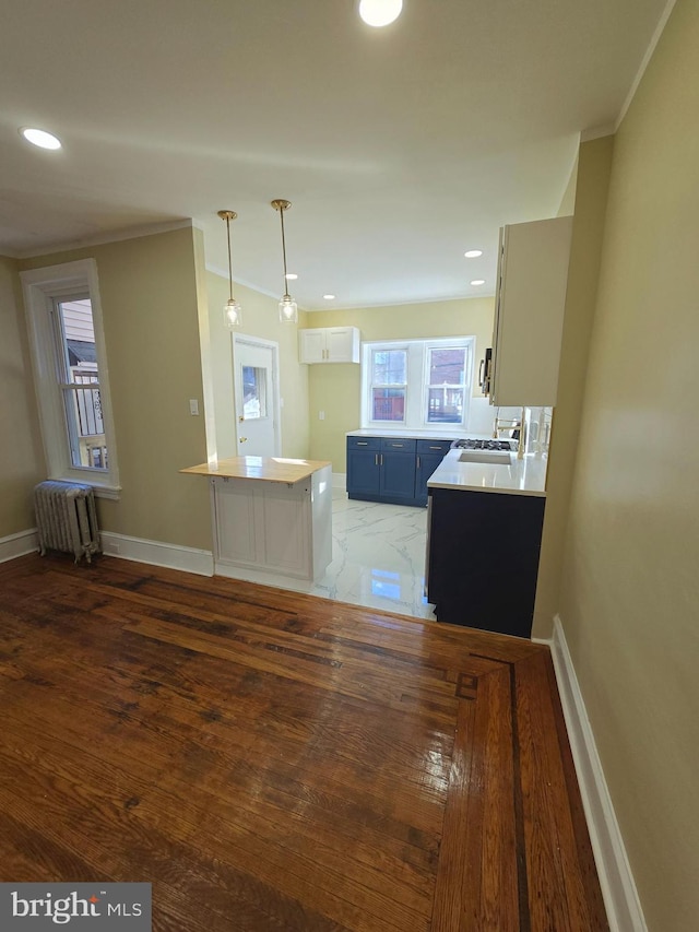 kitchen with sink, radiator, kitchen peninsula, pendant lighting, and white cabinets