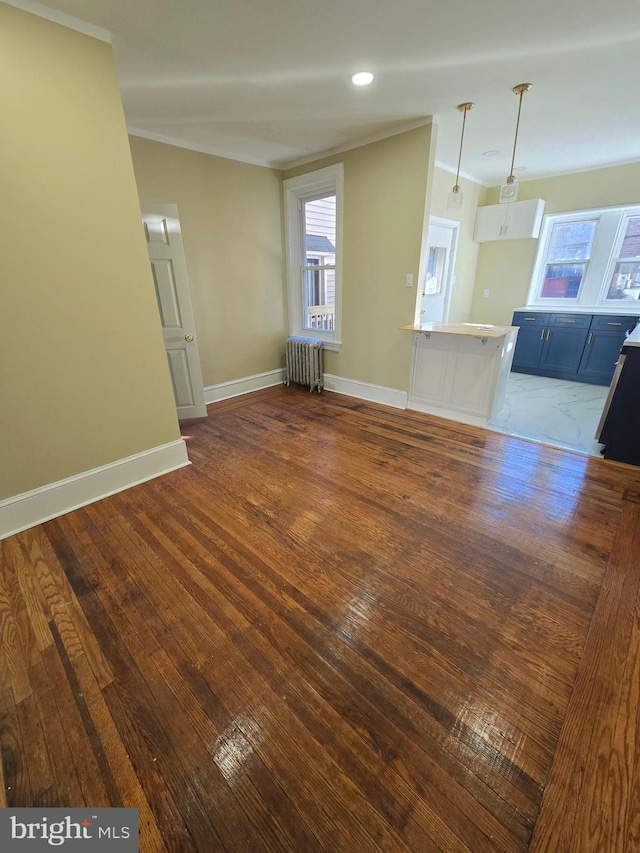 unfurnished living room with ornamental molding, plenty of natural light, dark wood-type flooring, and radiator heating unit