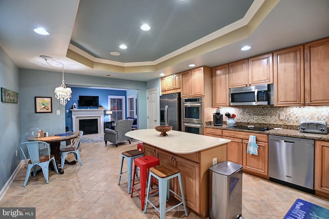 kitchen with pendant lighting, a raised ceiling, a kitchen bar, a center island, and stainless steel appliances