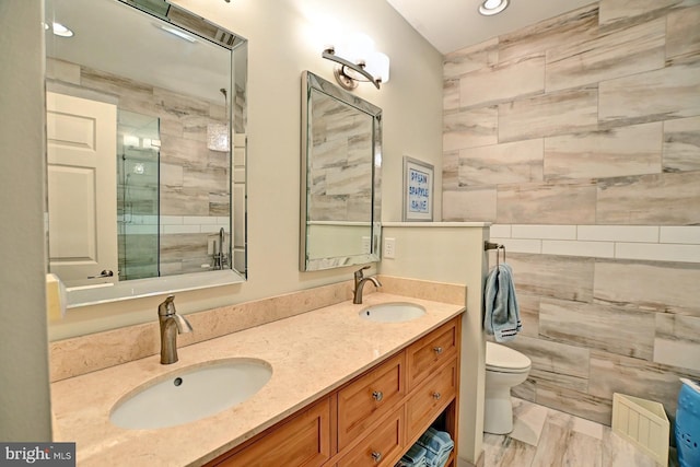 bathroom with vanity, a shower with door, tile walls, and toilet