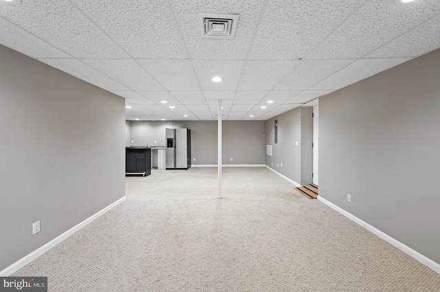 basement featuring a paneled ceiling and stainless steel fridge with ice dispenser