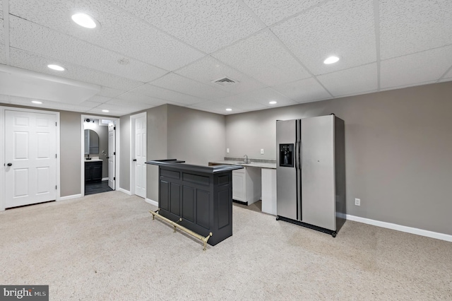 kitchen with sink, stainless steel fridge, white cabinetry, a kitchen island, and light carpet