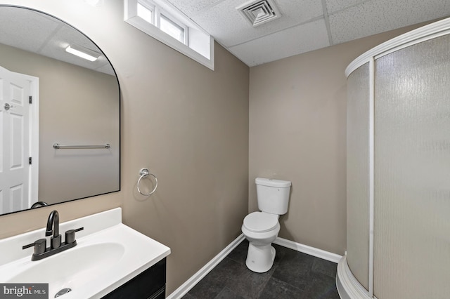 bathroom with a shower with door, vanity, a paneled ceiling, and toilet