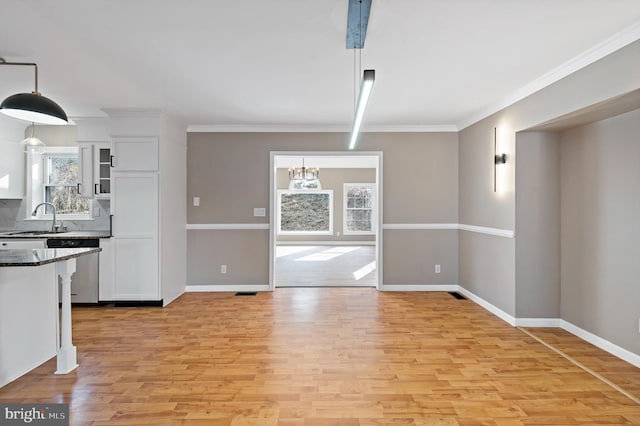 unfurnished dining area featuring crown molding, sink, a chandelier, and light wood-type flooring