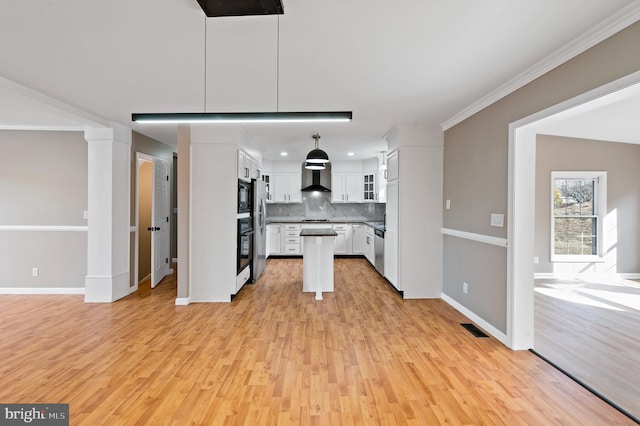 kitchen with appliances with stainless steel finishes, white cabinets, backsplash, hanging light fixtures, and wall chimney exhaust hood