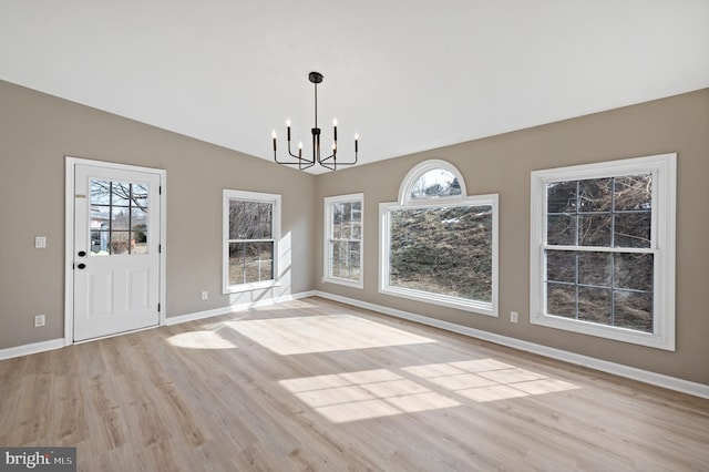 unfurnished dining area featuring a notable chandelier, vaulted ceiling, and light hardwood / wood-style floors