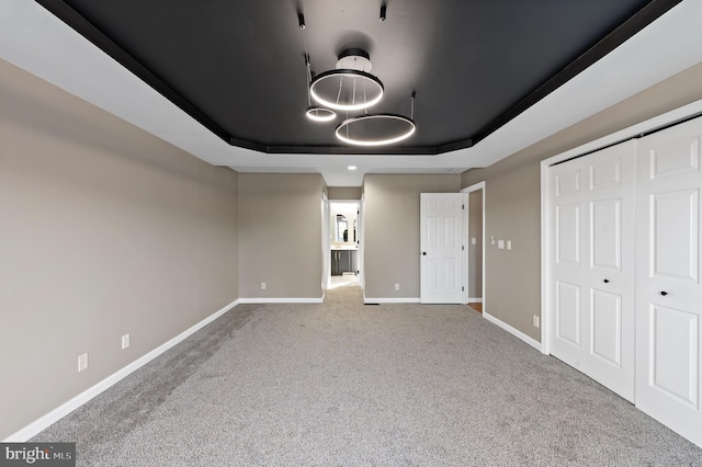 unfurnished bedroom with a closet, carpet, and a tray ceiling