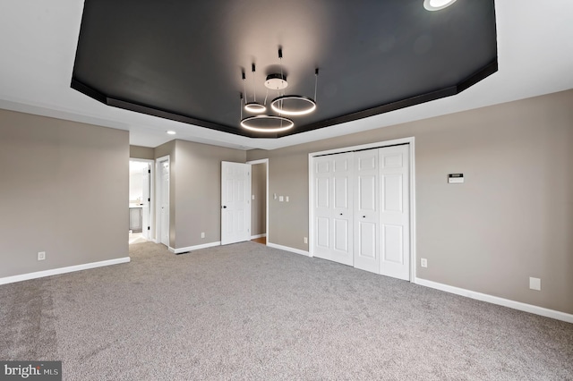 unfurnished bedroom featuring a raised ceiling, carpet floors, and a closet