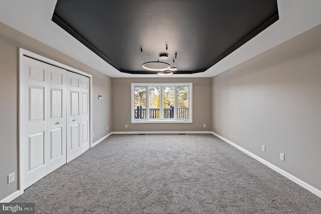 unfurnished bedroom with a raised ceiling, carpet floors, and a closet