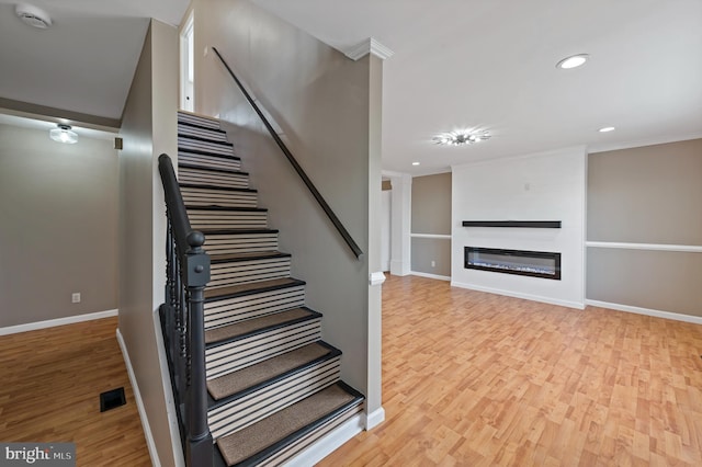 staircase featuring wood-type flooring, a large fireplace, and ornamental molding