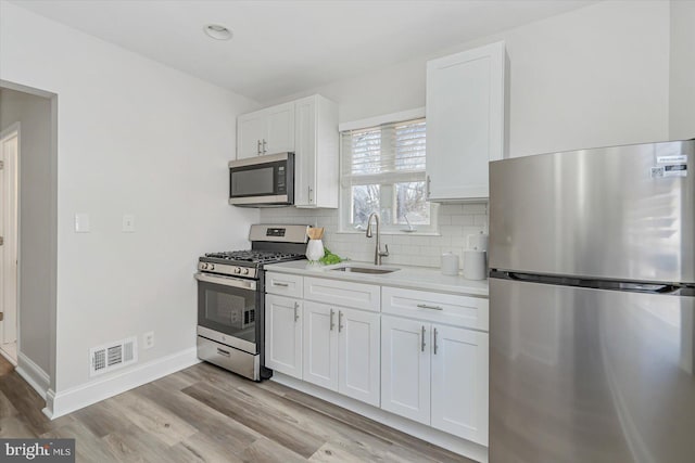 kitchen with stainless steel appliances, sink, decorative backsplash, and white cabinets