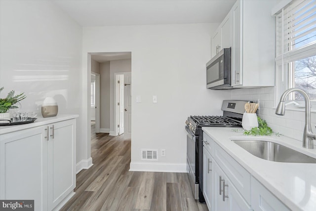 kitchen featuring white cabinetry, sink, backsplash, stainless steel appliances, and light wood-type flooring