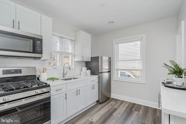 kitchen with sink, appliances with stainless steel finishes, backsplash, light hardwood / wood-style floors, and white cabinets