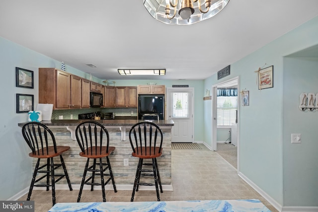 kitchen with backsplash, a notable chandelier, black appliances, a kitchen bar, and kitchen peninsula