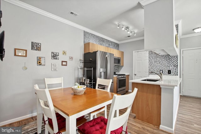 dining space featuring ornamental molding, sink, and light hardwood / wood-style flooring