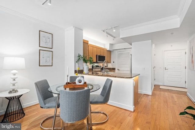 dining space featuring crown molding, sink, track lighting, and light hardwood / wood-style floors