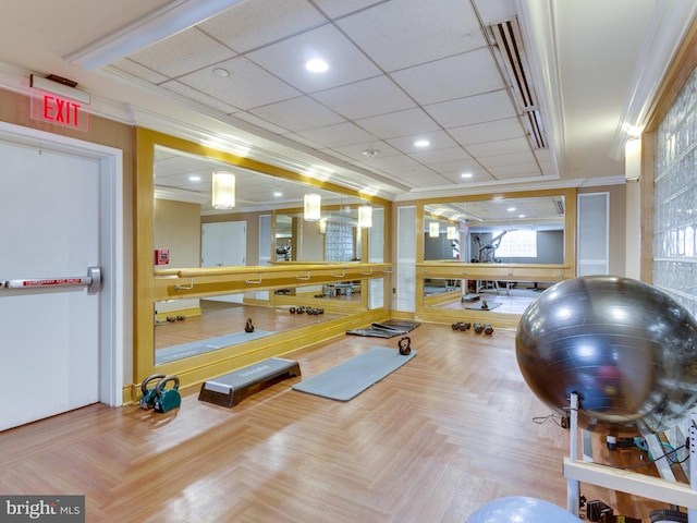 workout area with a drop ceiling, crown molding, and light parquet floors