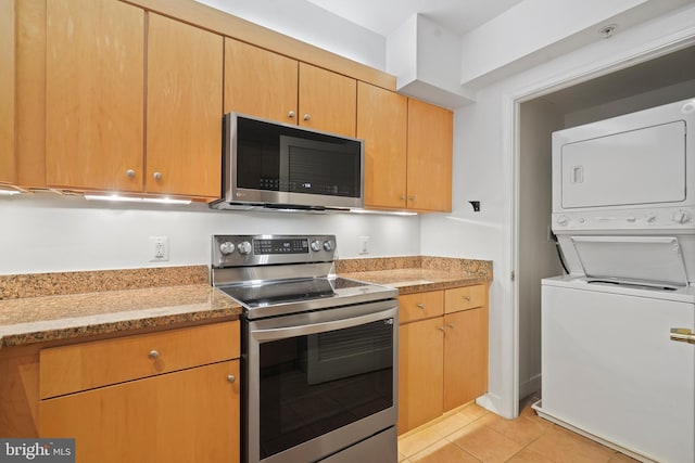 kitchen with stacked washer and dryer, appliances with stainless steel finishes, light stone countertops, and light tile patterned floors