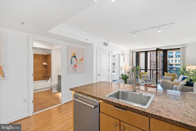 kitchen with dishwasher, sink, dark stone countertops, track lighting, and light hardwood / wood-style flooring