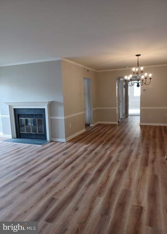 unfurnished living room featuring hardwood / wood-style flooring, crown molding, and a chandelier