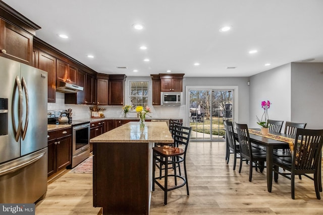 kitchen with a kitchen island, backsplash, stainless steel appliances, light stone countertops, and light wood-type flooring