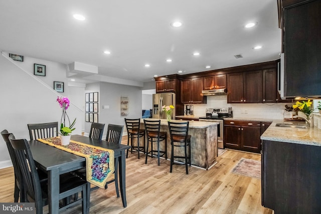 kitchen featuring sink, light hardwood / wood-style flooring, appliances with stainless steel finishes, light stone counters, and a kitchen island