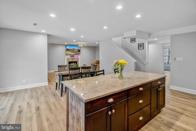 kitchen featuring dark brown cabinetry, light stone countertops, a kitchen island, and light hardwood / wood-style floors