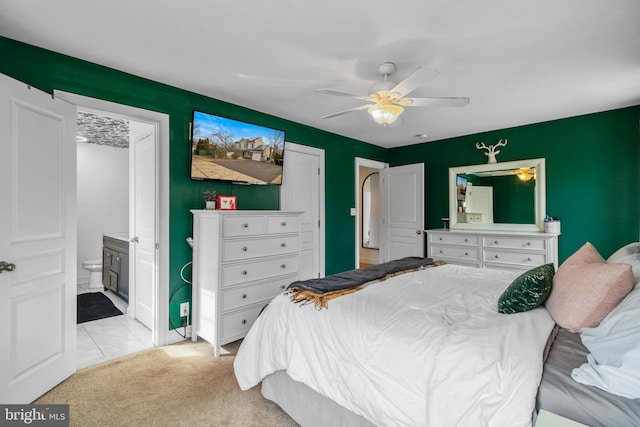 bedroom featuring ensuite bathroom, light colored carpet, and ceiling fan