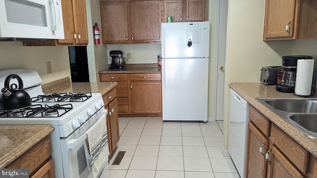 kitchen featuring white appliances, light tile patterned floors, visible vents, a sink, and brown cabinets