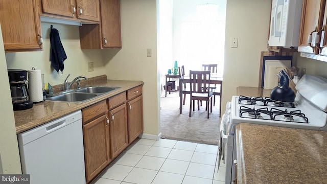 kitchen with light carpet, brown cabinets, a sink, white appliances, and light tile patterned floors