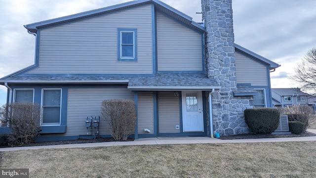 view of front of house with a front lawn, roof with shingles, and a chimney