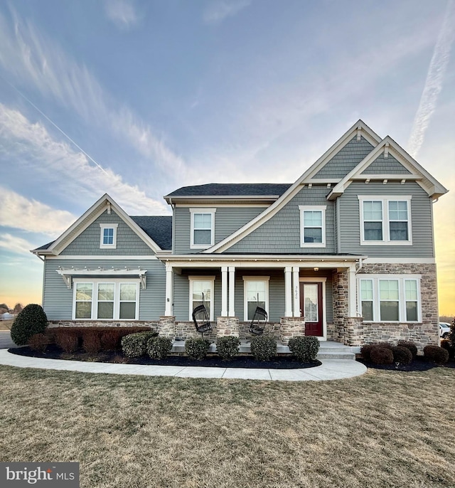 craftsman house with a front yard, stone siding, and covered porch