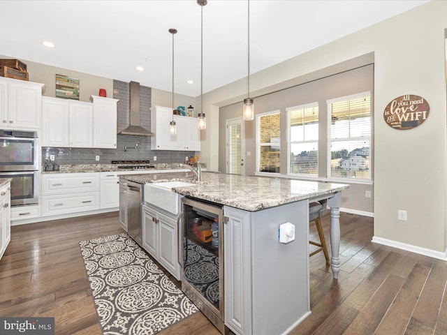 kitchen with tasteful backsplash, beverage cooler, wall chimney exhaust hood, stainless steel appliances, and a sink