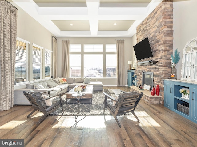 living room with a towering ceiling, a fireplace, coffered ceiling, and wood finished floors