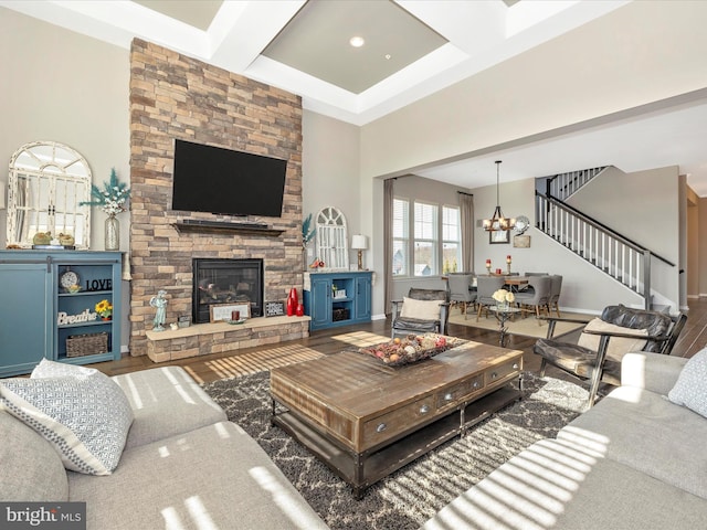 living room featuring stairway, an inviting chandelier, a stone fireplace, wood finished floors, and coffered ceiling