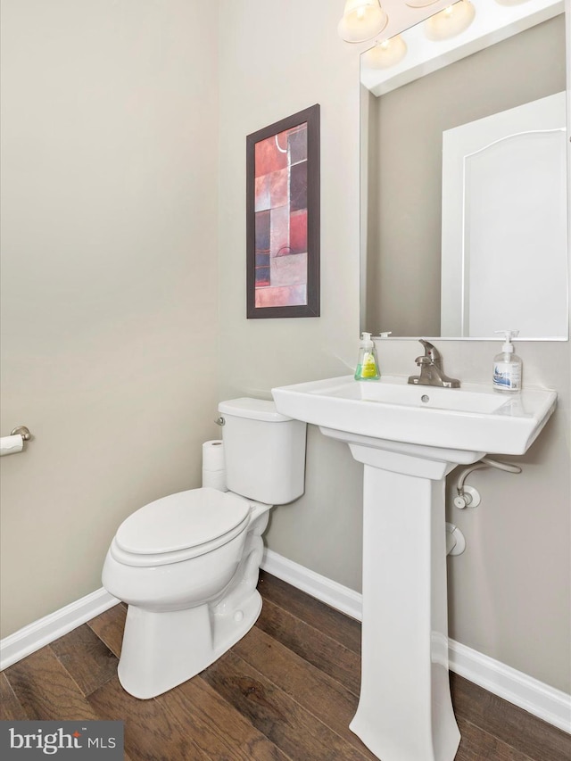 half bathroom with toilet, a sink, baseboards, and wood finished floors