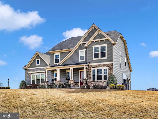 craftsman-style home with stone siding, a porch, and a front yard