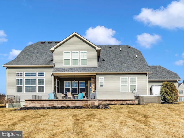 back of house with roof with shingles, a lawn, and a patio