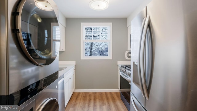 clothes washing area with stacked washer / dryer, light wood-style flooring, laundry area, and baseboards