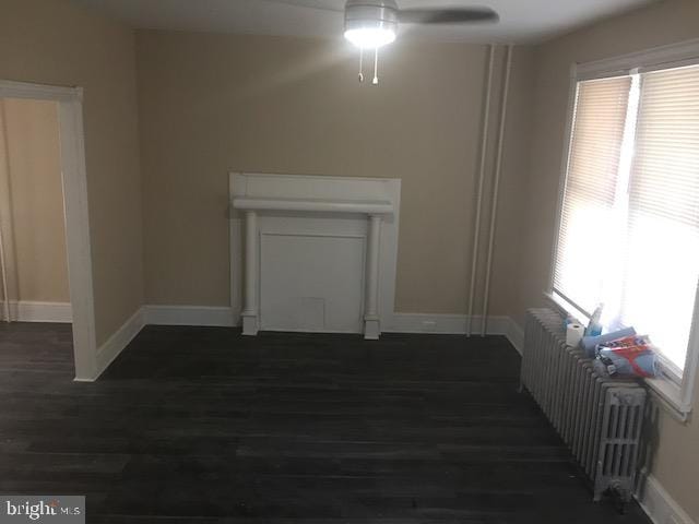 unfurnished living room with dark hardwood / wood-style flooring, a wealth of natural light, radiator heating unit, and ceiling fan